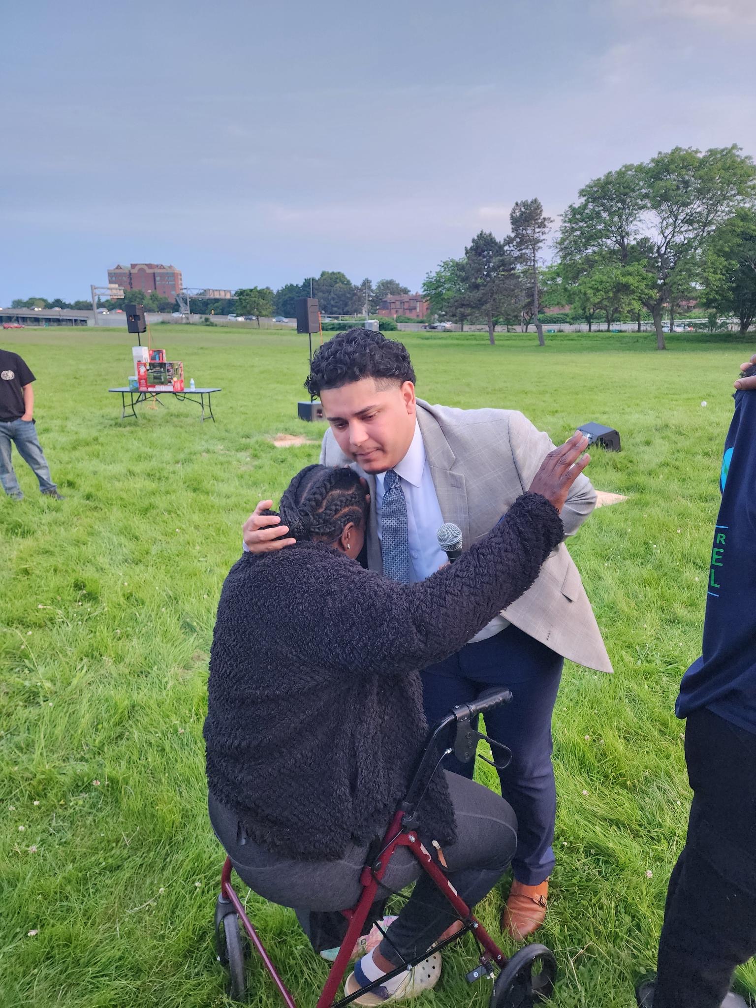 Izaiah Diaz kneeling in prayer with a child at a Buffalo outdoor gathering