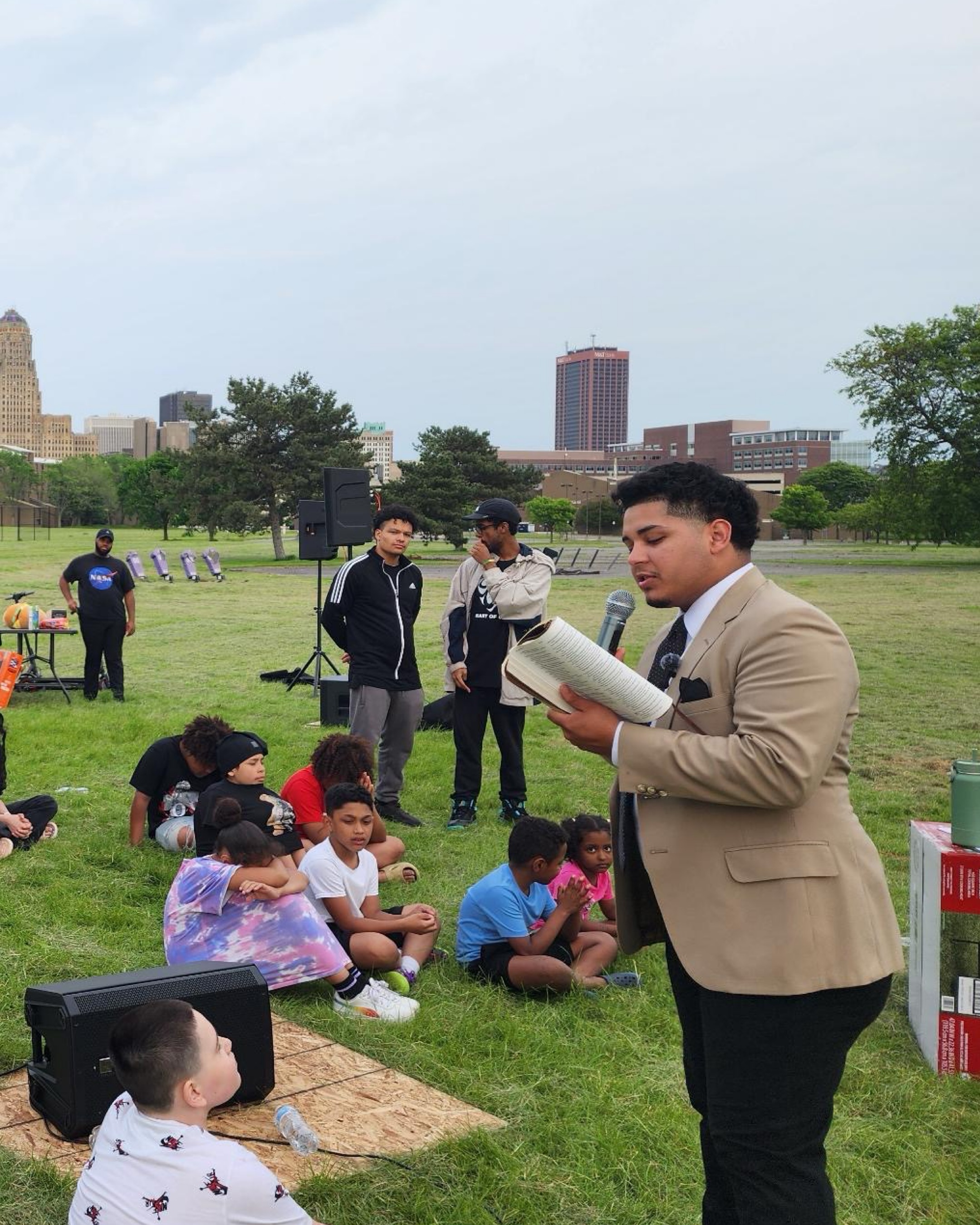 Izaiah preaching from an open Bible to seated youth in a Buffalo park