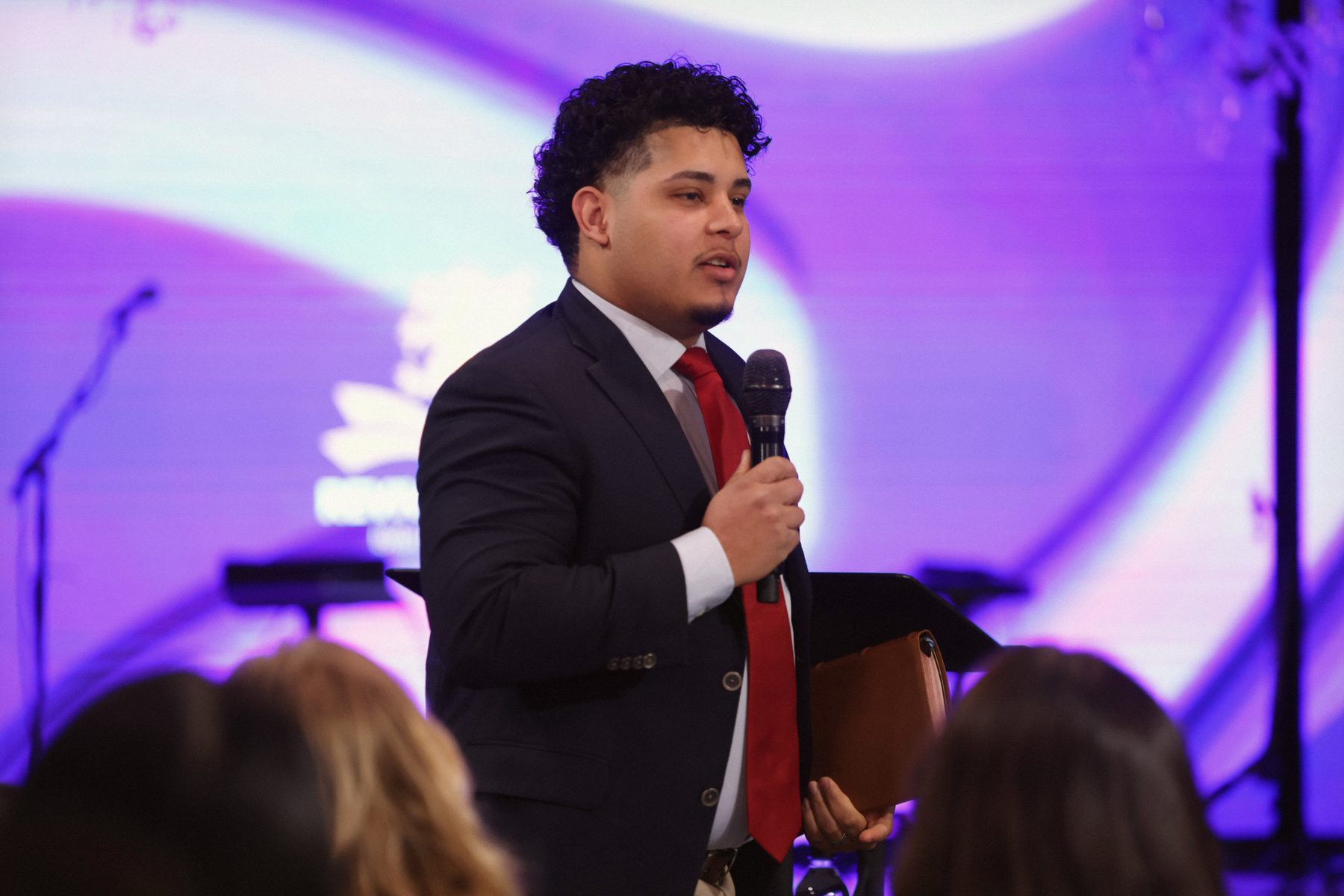 Preaching from the stage in navy suit and red tie