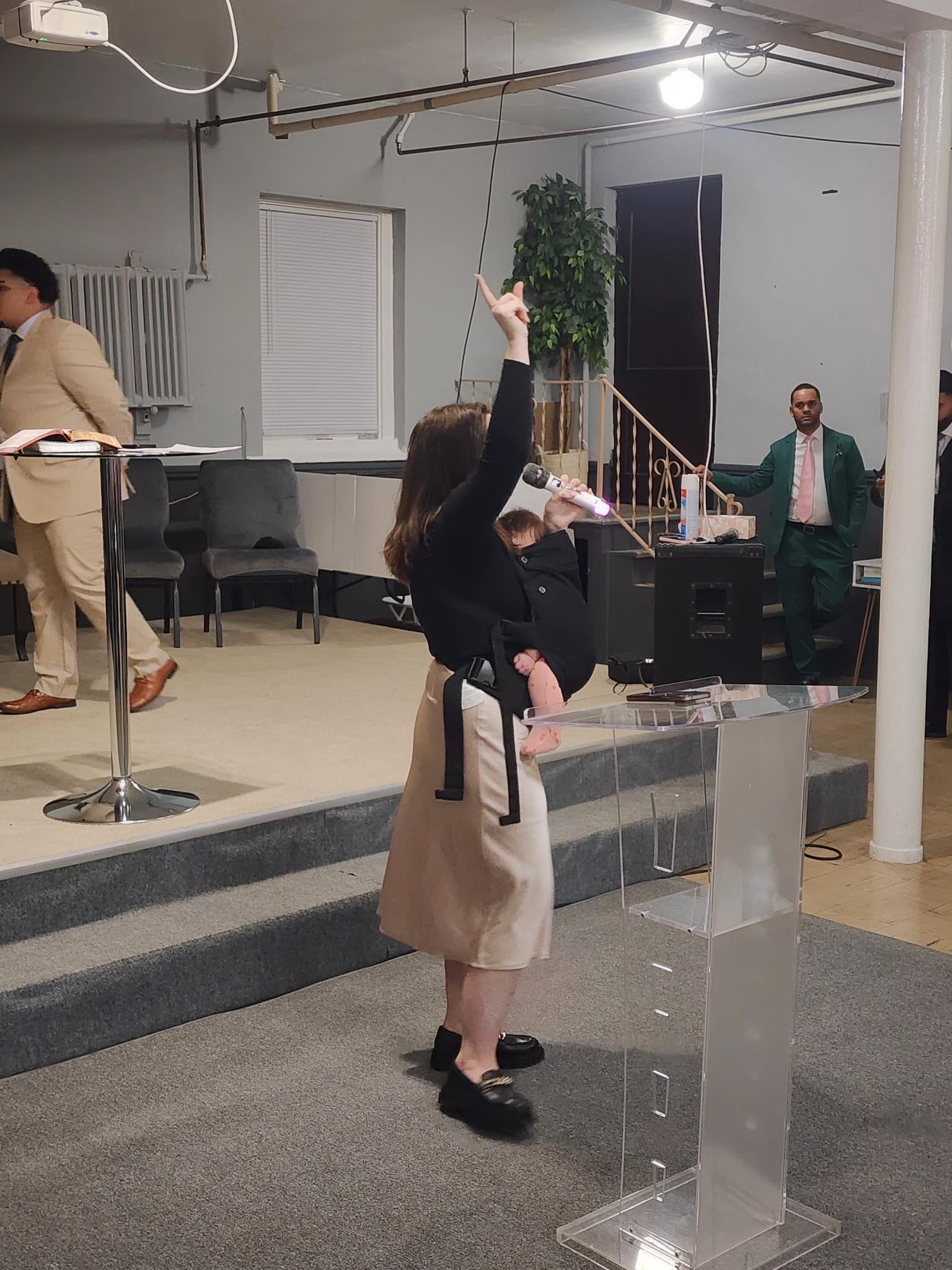Kaylie Diaz worshipping with her hand raised, baby in carrier